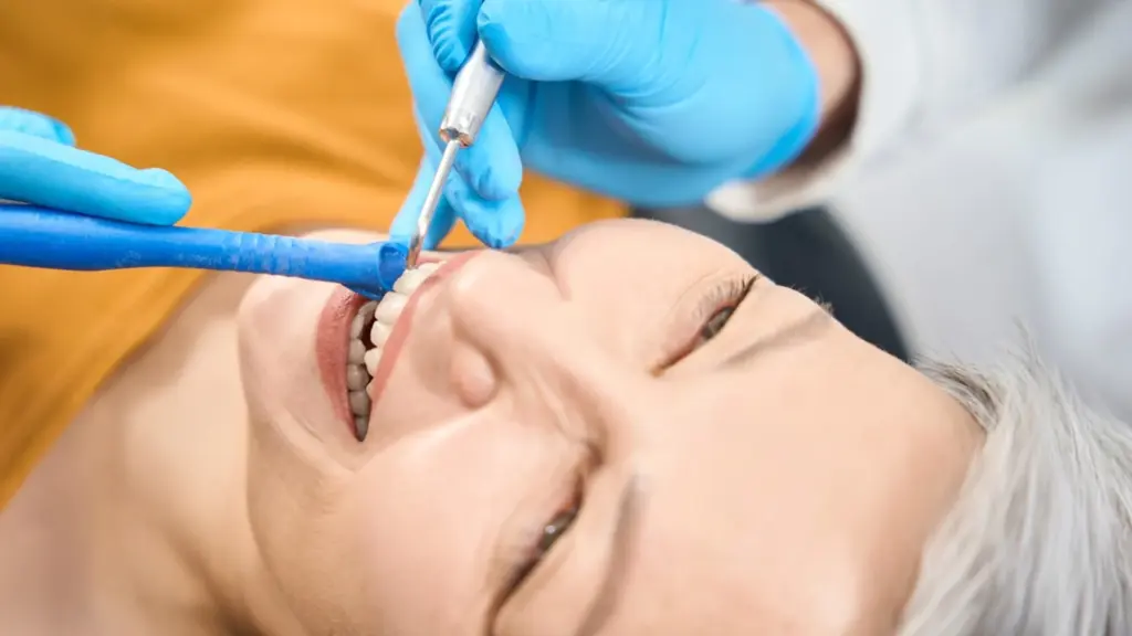 A dentist using a mouth mirror to inspect a female patient's teeth during a routine dental check-up.