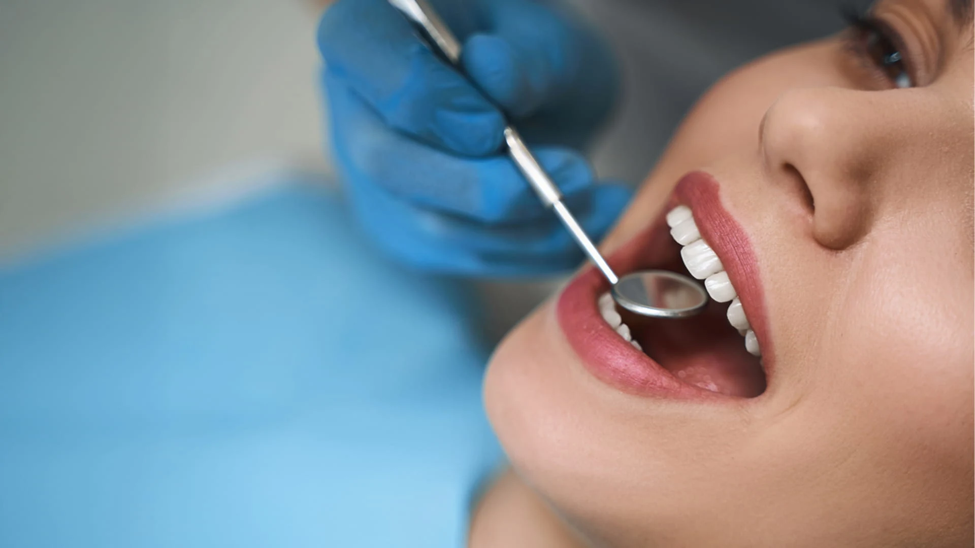 Close-up of a dentist in blue gloves performing a dental examination on a patient using a dental probe and suction tool.