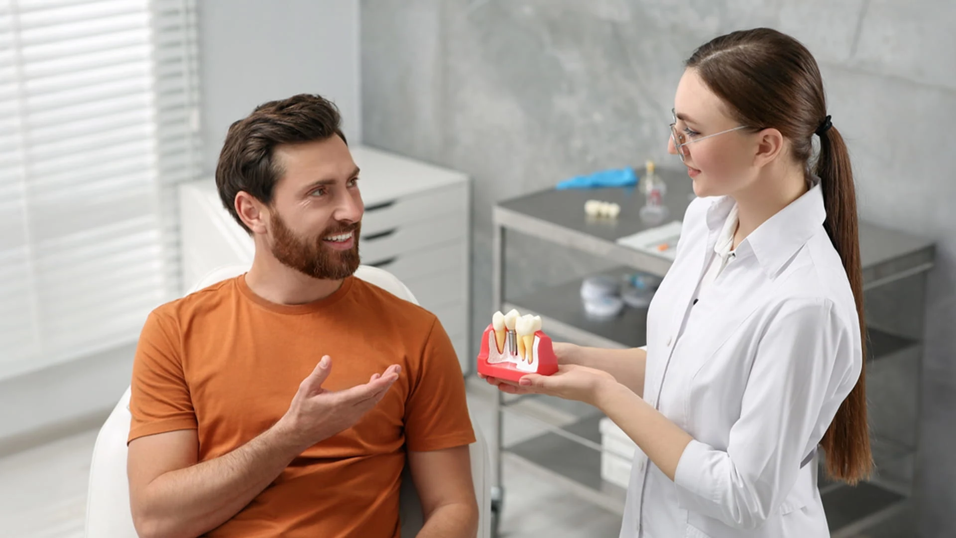 A female dentist at Yarralumla Dental Care shows a dental implant model to a smiling male patient during a consultation.