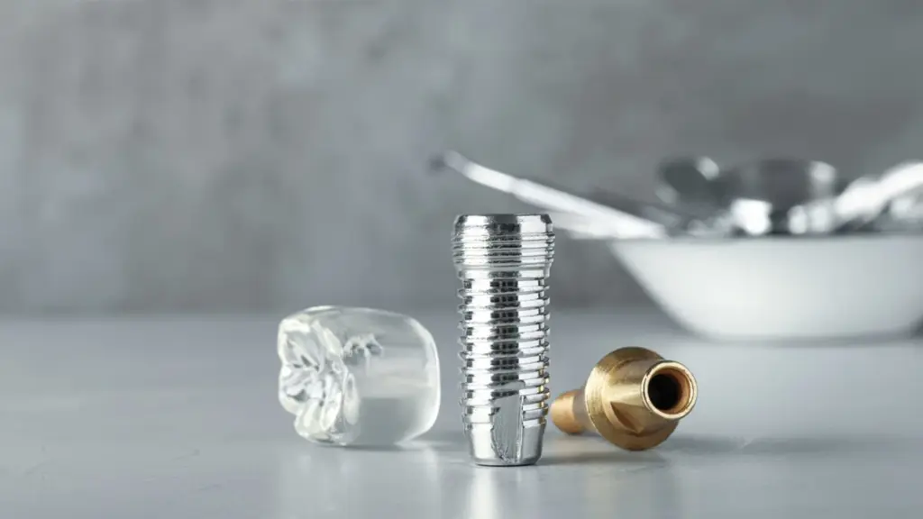 A close-up view of a metal dental implant screw, an abutment, and a clear dental crown model on a clinical surface at Yarralumla Dental Care.